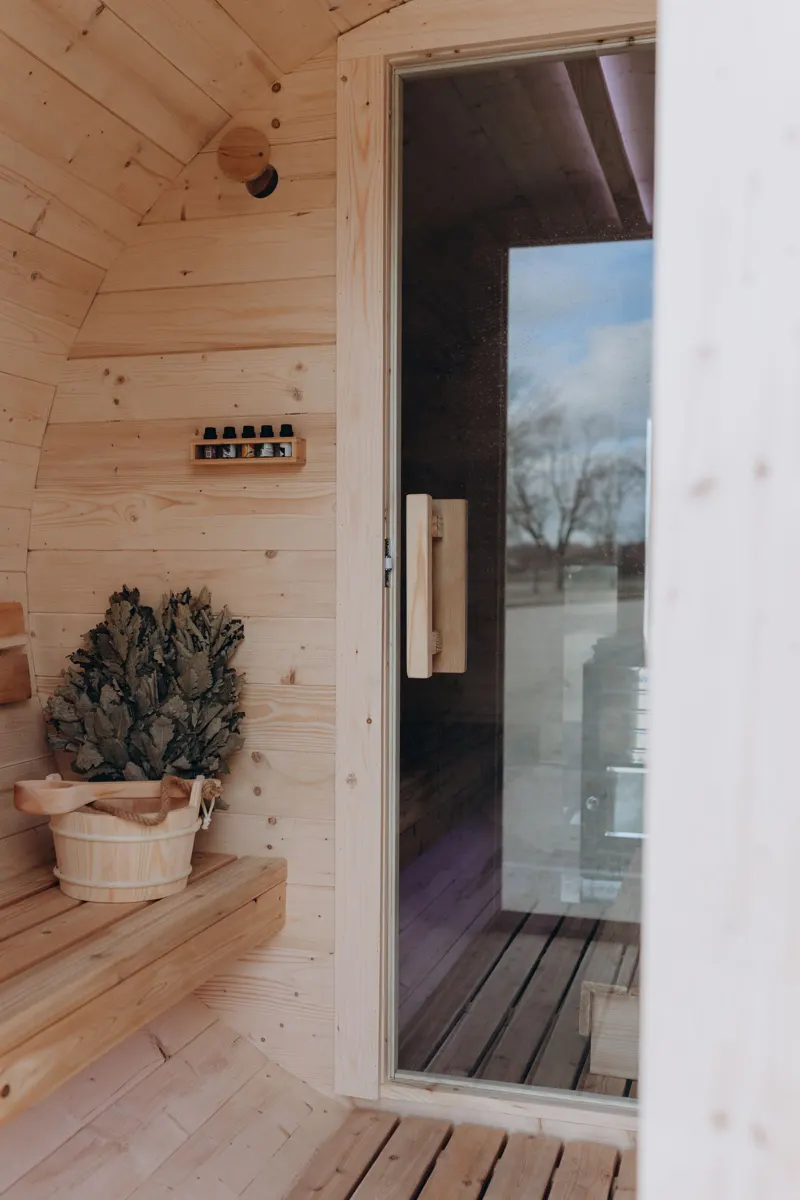 View from inside the cedar sauna out through the glass door, with a whisk and bucket on the bench